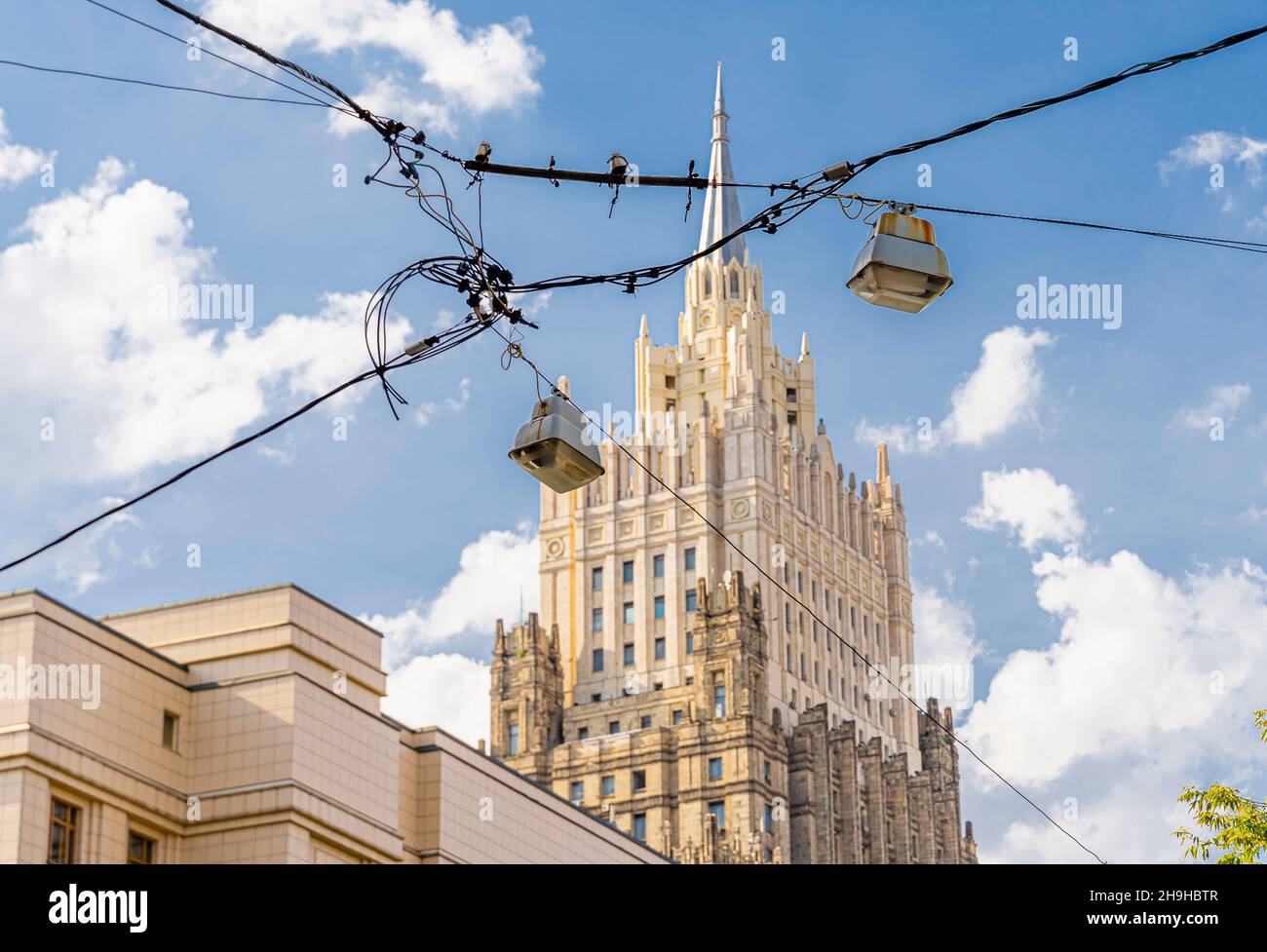 Old hanging streetlamps on cables or wires suspended above the road. One of Moscow Stalinist highrises in background. Russia Stock Photo