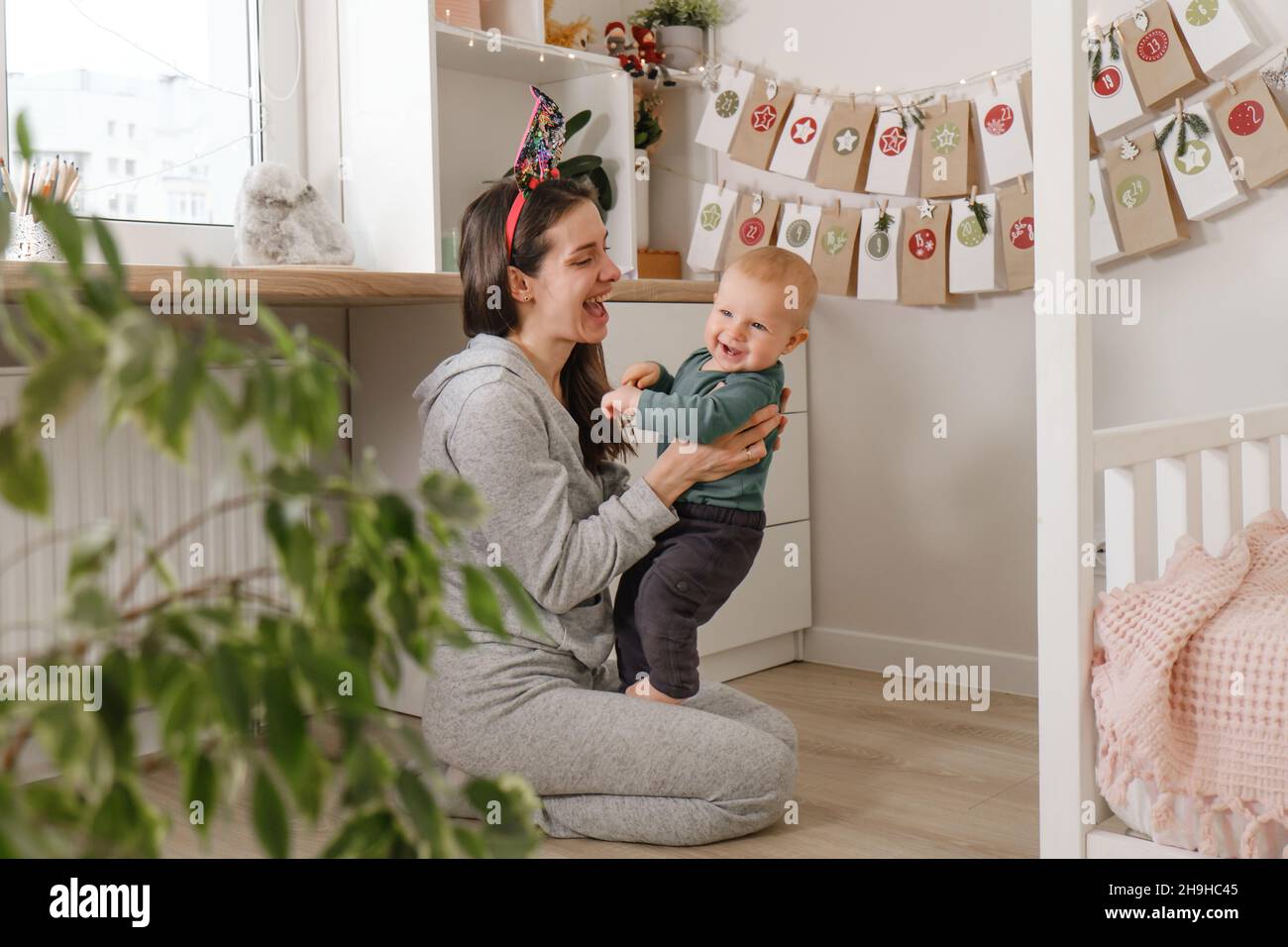 Mother with infant child having fun Christmas advent calendar tasks and gifts. Baby boy excited about festive surprise and play at home. Family Stock Photo