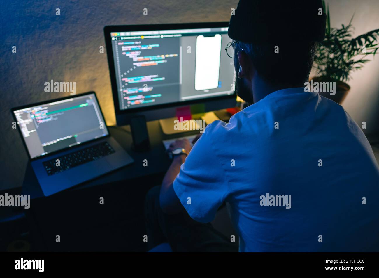 Young man mobile developer writes program code on a computer, programmer work in home office. Stock Photo
