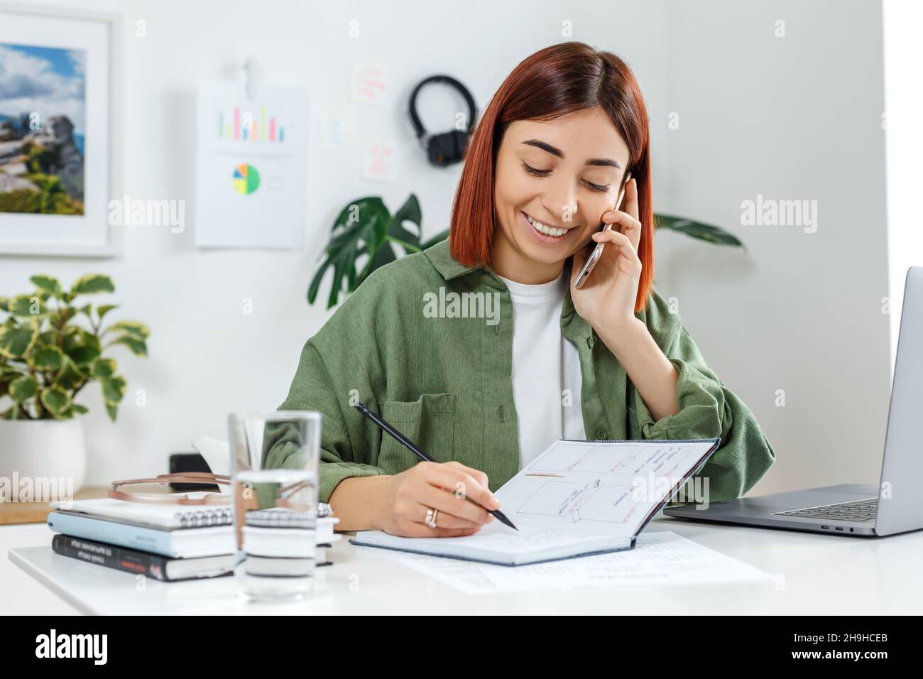 Woman remotely working at home with laptop computer. Young businesswoman talking by phone. Concept of online business or communication, home office an Stock Photo