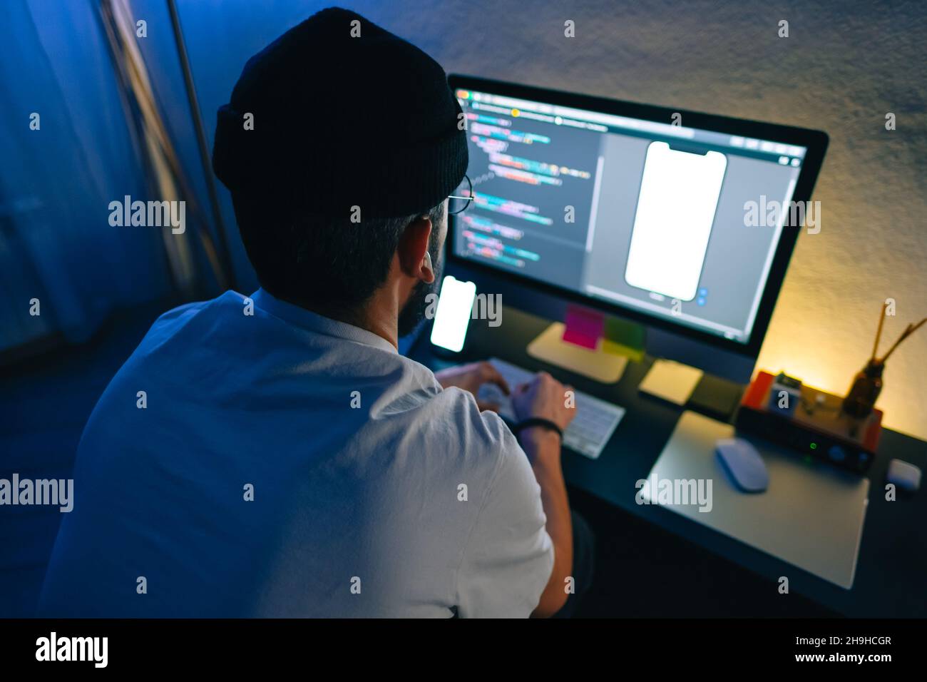 Young man mobile developer writes program code on a computer, programmer work in home office. Stock Photo