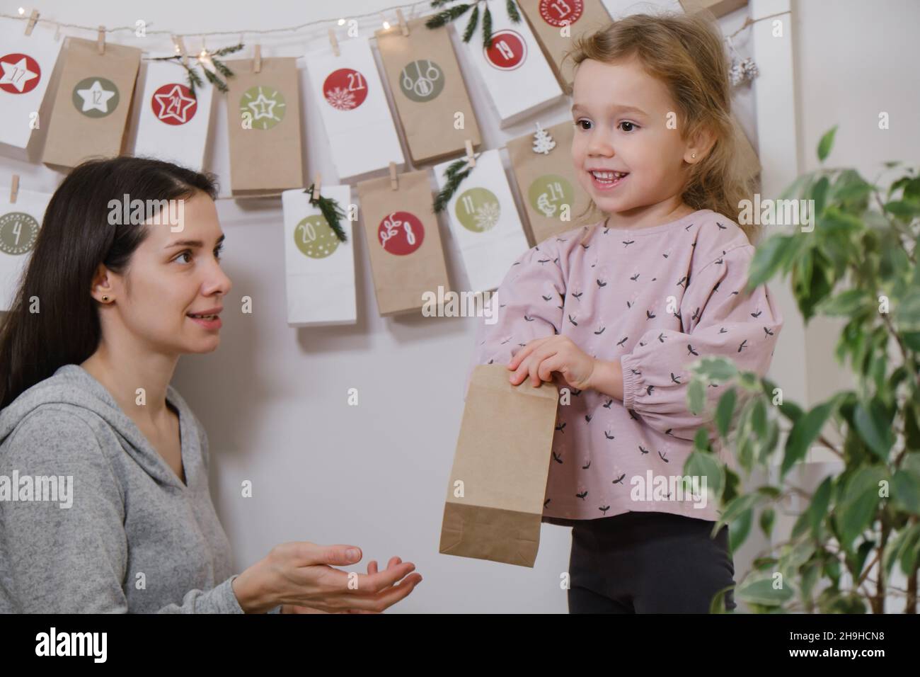 Mother with child opening Christmas advent calendar tasks and gifts. Toddler girl excited about festive surprise in craft bag at home. Family Stock Photo