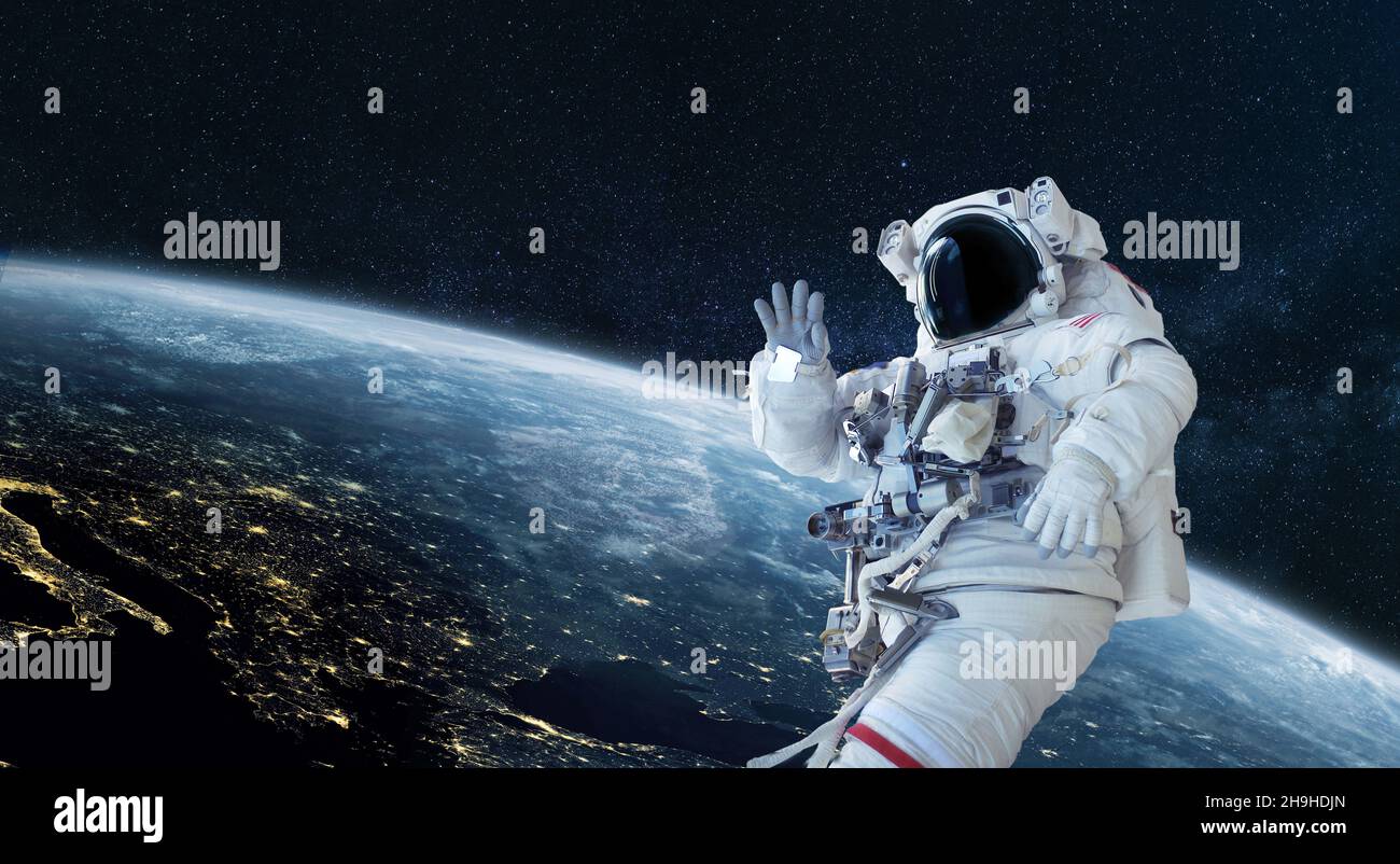 Space man astronaut greets and waves his hand in space on a background ...
