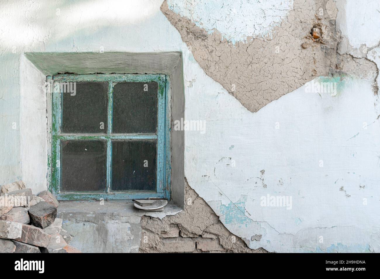 Small framed dusty window in a wall with disintegrated plastering showing layers of сement and brick. Dirty unwashed rectangular window. Stock Photo