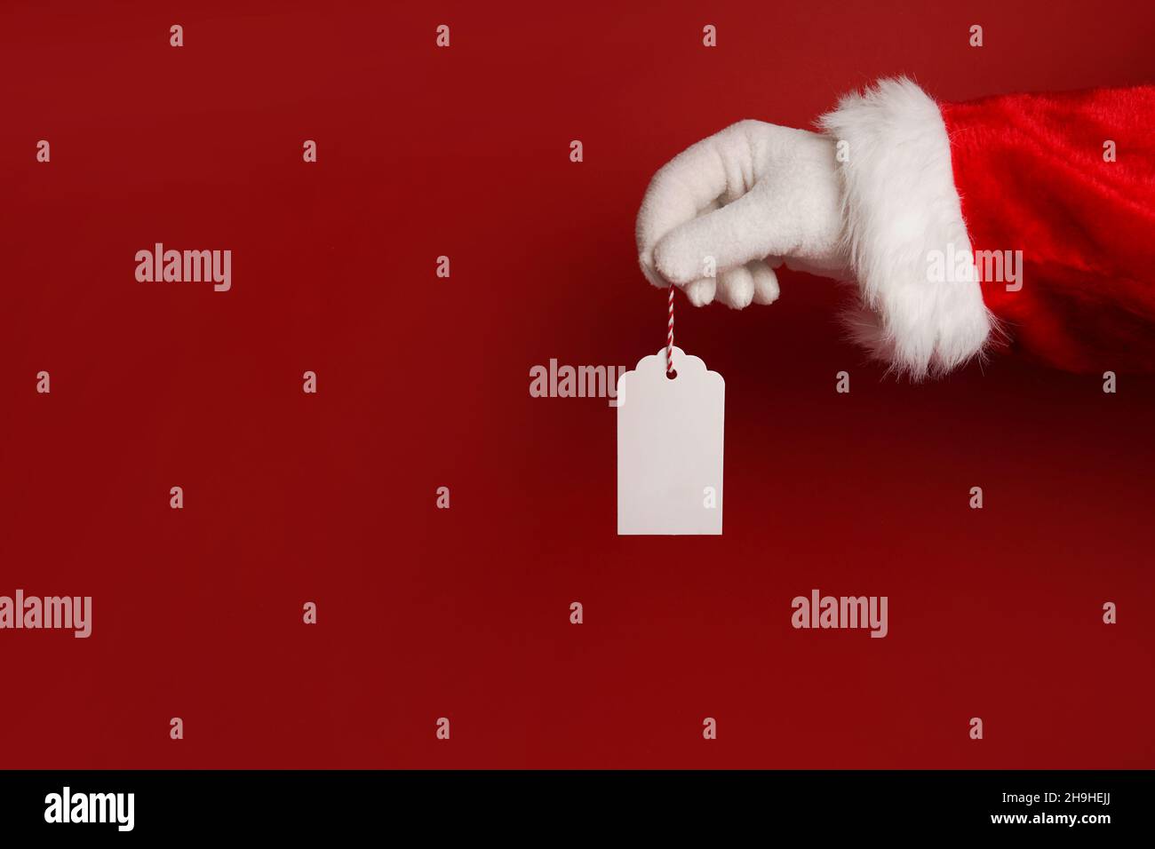 santa claus hand holding white blank tag label on red background with ...