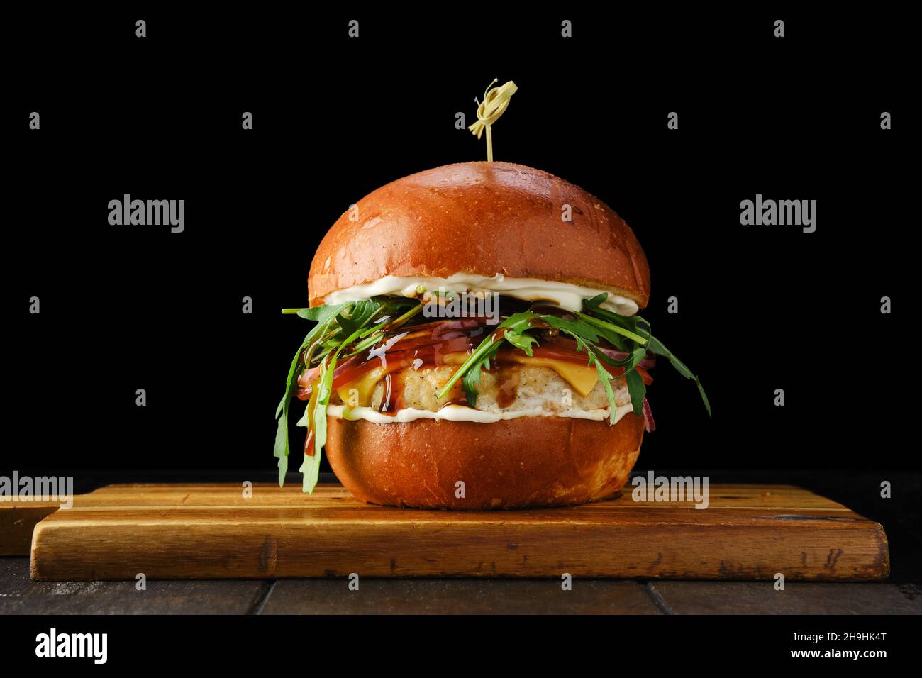 Burger with chicken patty teriyaki sauce on wooden serving board over black background Stock Photo