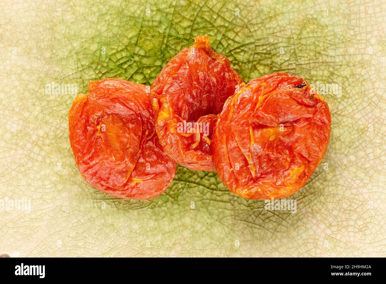 Several sweet dry apricots, close-up on a ceramic dish, top view. Stock Photo