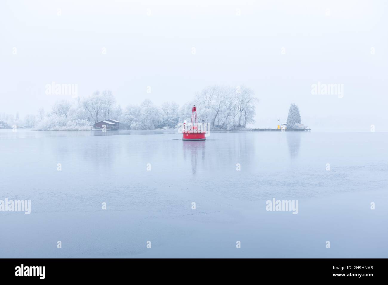 A big red buoy in the frozen water of the citylake 'the Nieuwe Meer lake in Amsterdam. Reflection in the ice and water and frozen harbour trees and fo Stock Photo