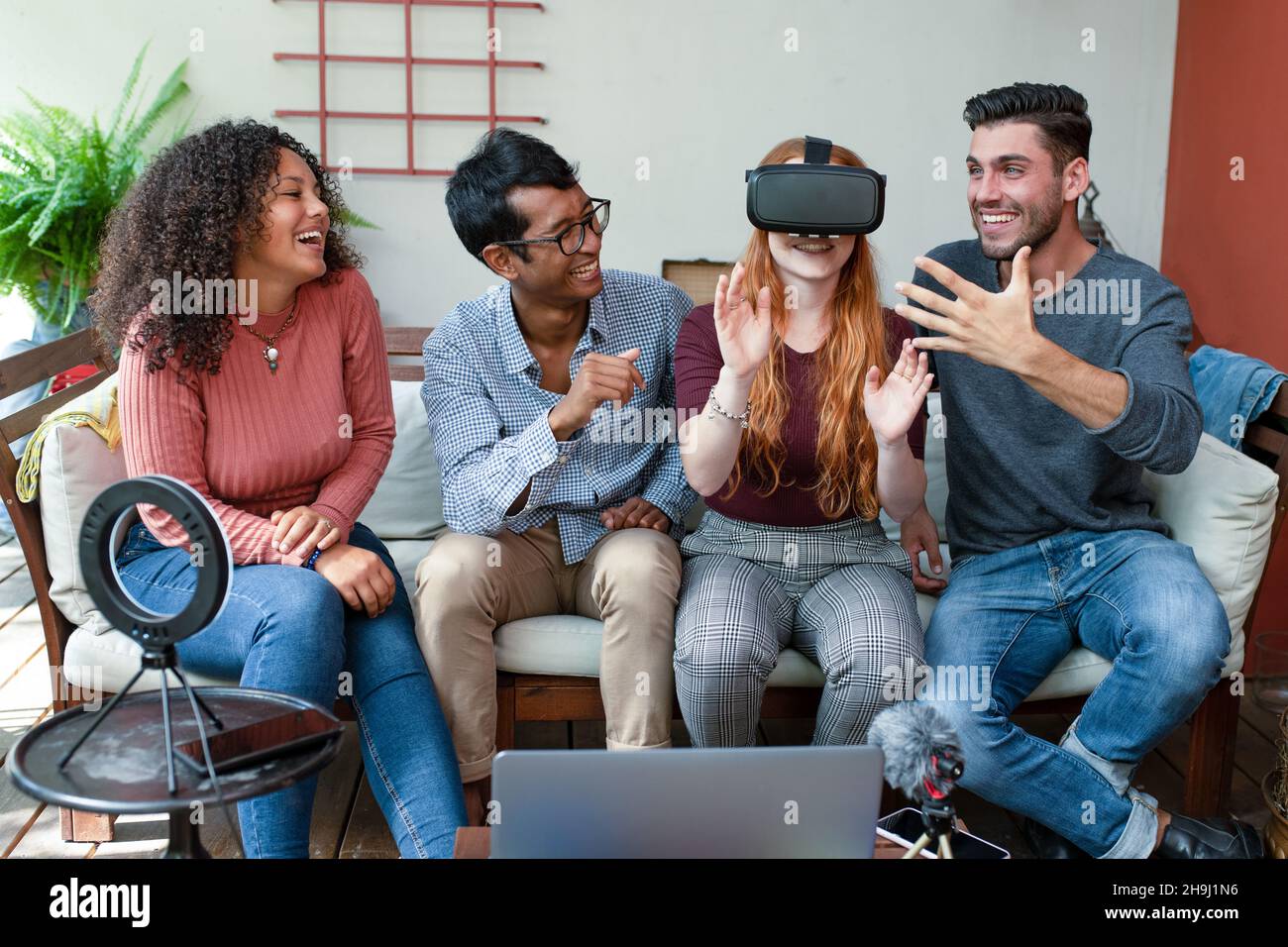 group of young friends experiencing virtual reality with headset, blogger making streaming podcast with ring light, microphone and laptop explaining t Stock Photo