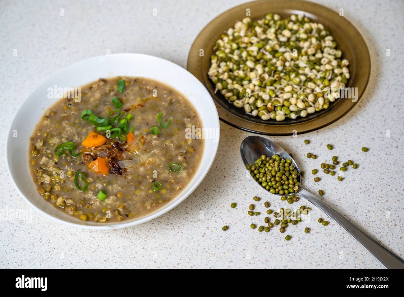 Mungo beans soup in white plate, spoon with dry mungo seed (vigna radiata), sprouted mungo in brown plate on cutting board. Stock Photo