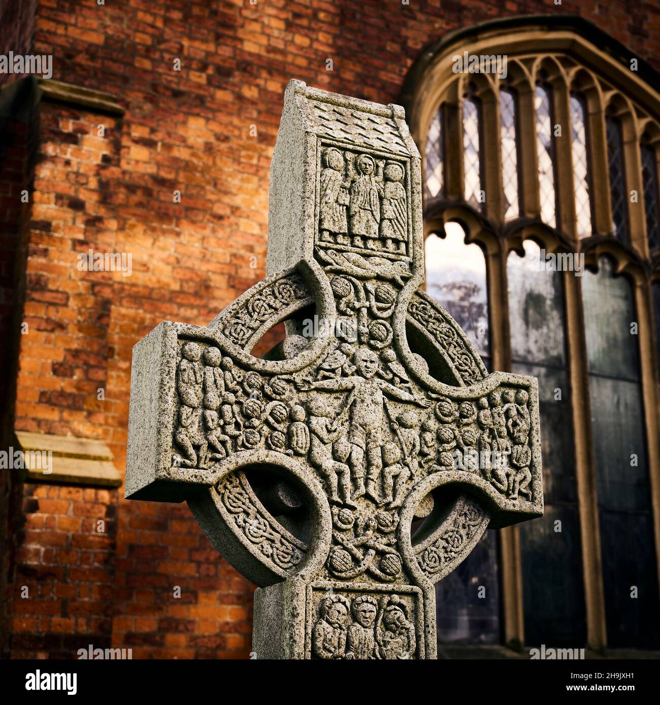 Celtic Cross in churchyard set against stained glass window of church Stock Photo