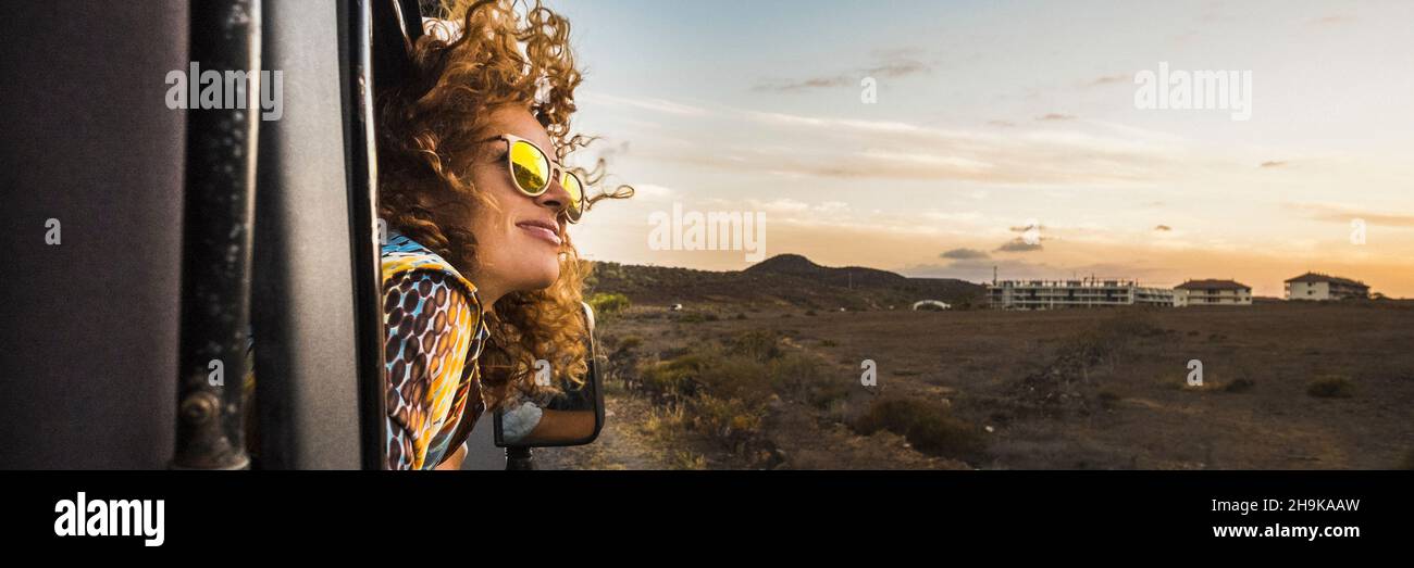 Happy woman traveling on car outside the windows enjoying wind and freedom admire the sunset. Banner header for travel lifestyle concept Stock Photo