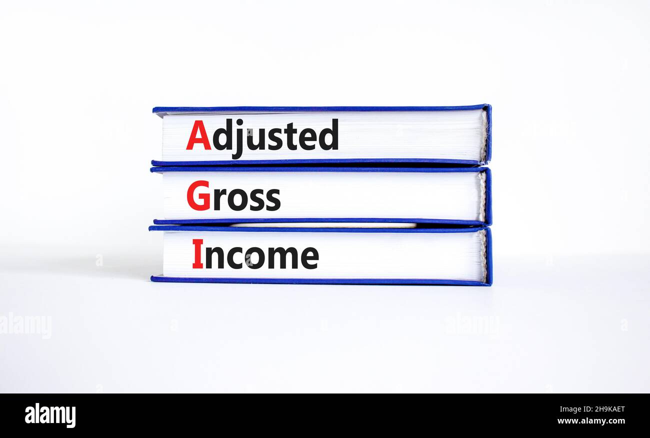 AGI adjusted gross income symbol. Concept words AGI adjusted gross income on books. Beautiful white table, white background, copy space. Business and Stock Photo