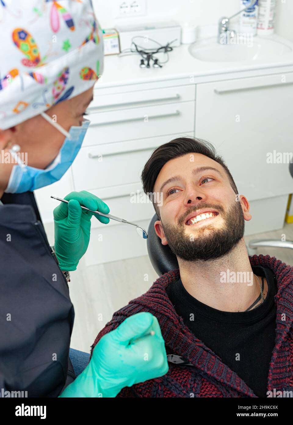 Female dentist examines a man patient in a dental office using professional tools and personal protective equipment. Stock Photo