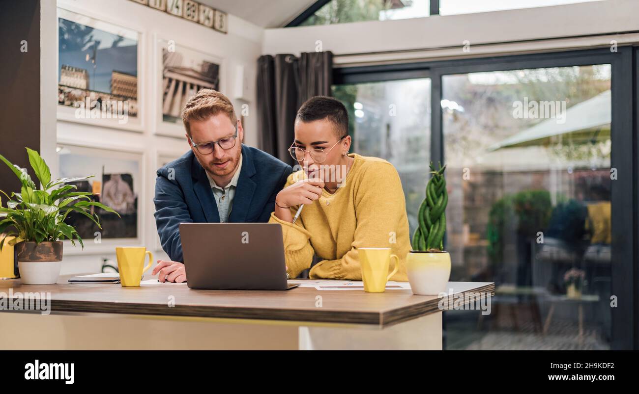 Young successful mixed races couple sitting in living room or kitchen discussing new home project using laptop working and planing calculating home fi Stock Photo