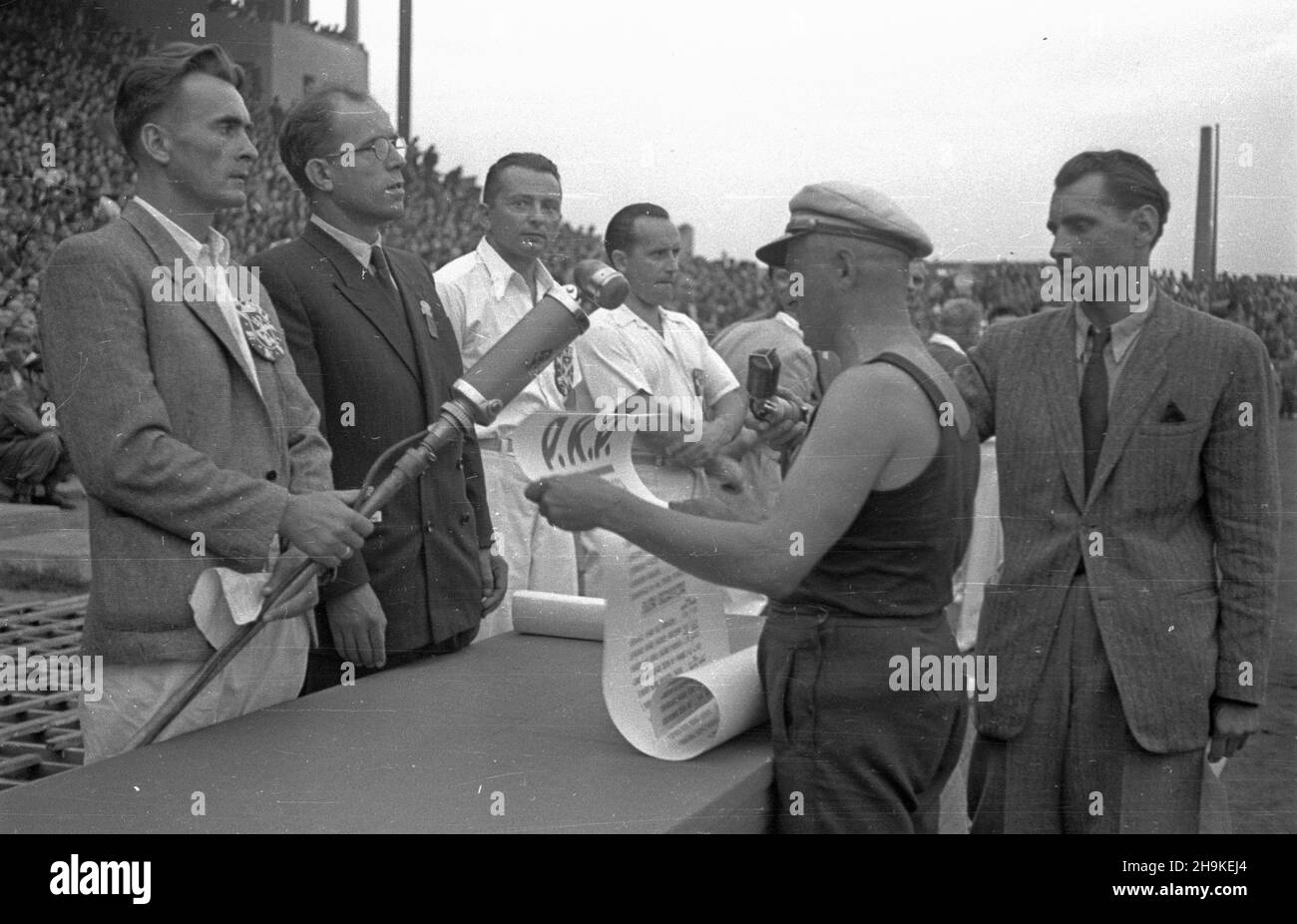 Warszawa, 1948-08-19. Pierwsze ogólnopolskie Igrzyska Sportowe Zwi¹zków Zawodowych (19-22.VIII) na stadionie Wojskowego Klubu Sportowego Legia, w których rywalizowali w 11 dyscyplinach reprezentanci 17 zwi¹zków zawodowych. Nz. m.in. przewodnicz¹cy Komisji Centralnej Zwi¹zków Zawodowych Kazimierz Witaszewski (w okularach) s³ucha przemówienia delegata Kolejarzy. Z prawej sprawozdawca Polskiego Radia Tadeusz Pyszkowski. ka PAP Warsaw, Aug. 19, 1948. The first national Trade Union Sports Competition (Aug. 19-22) held at the stadium of the Military Sports Club Legia. The event brought togeth Stock Photo