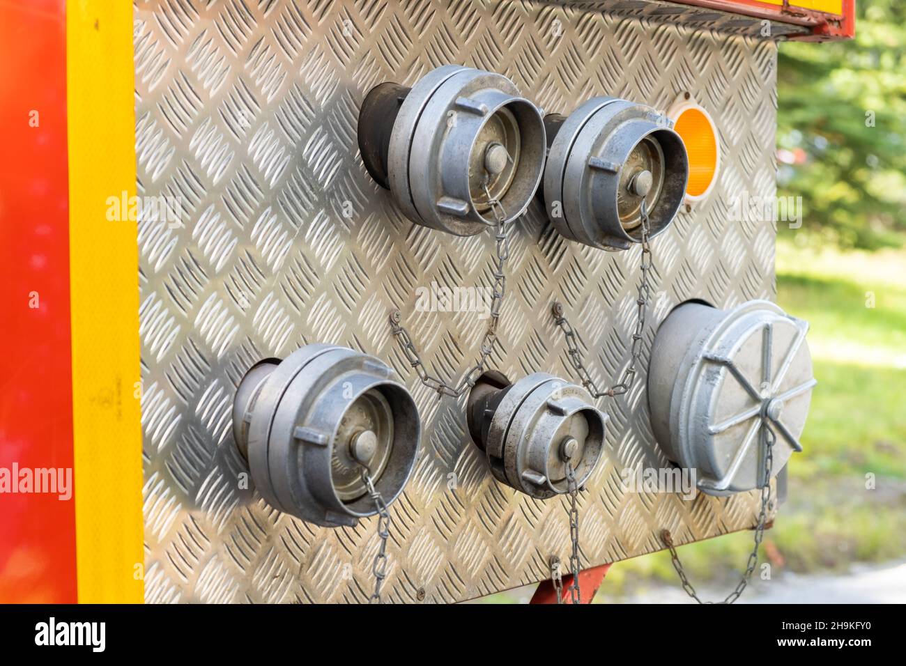 Hose plugs on metal side of contemporary fire engine standing in street near green park on summer day extreme close view Stock Photo