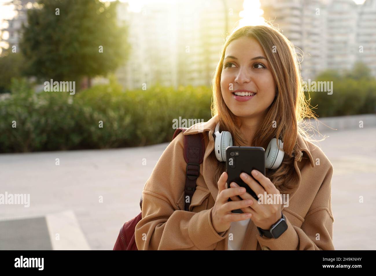 Cool modern teenage girl thinking and looking to the side holding smartphone outdoors. Copy space. Stock Photo