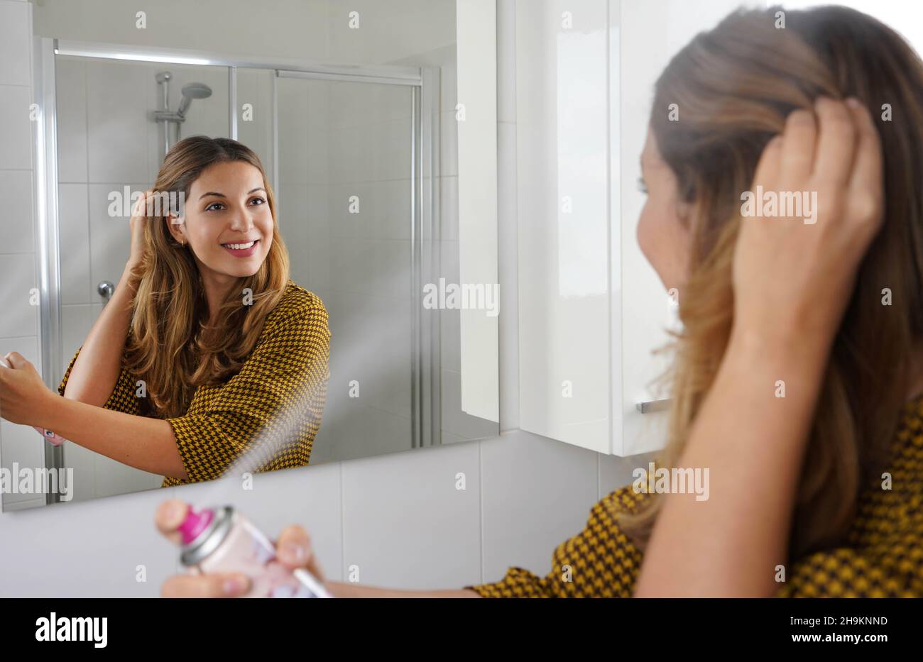 Young woman applying dry shampoo on her hair before going out. Fast and easy way to covering grey hair with instant spray dye. Stock Photo