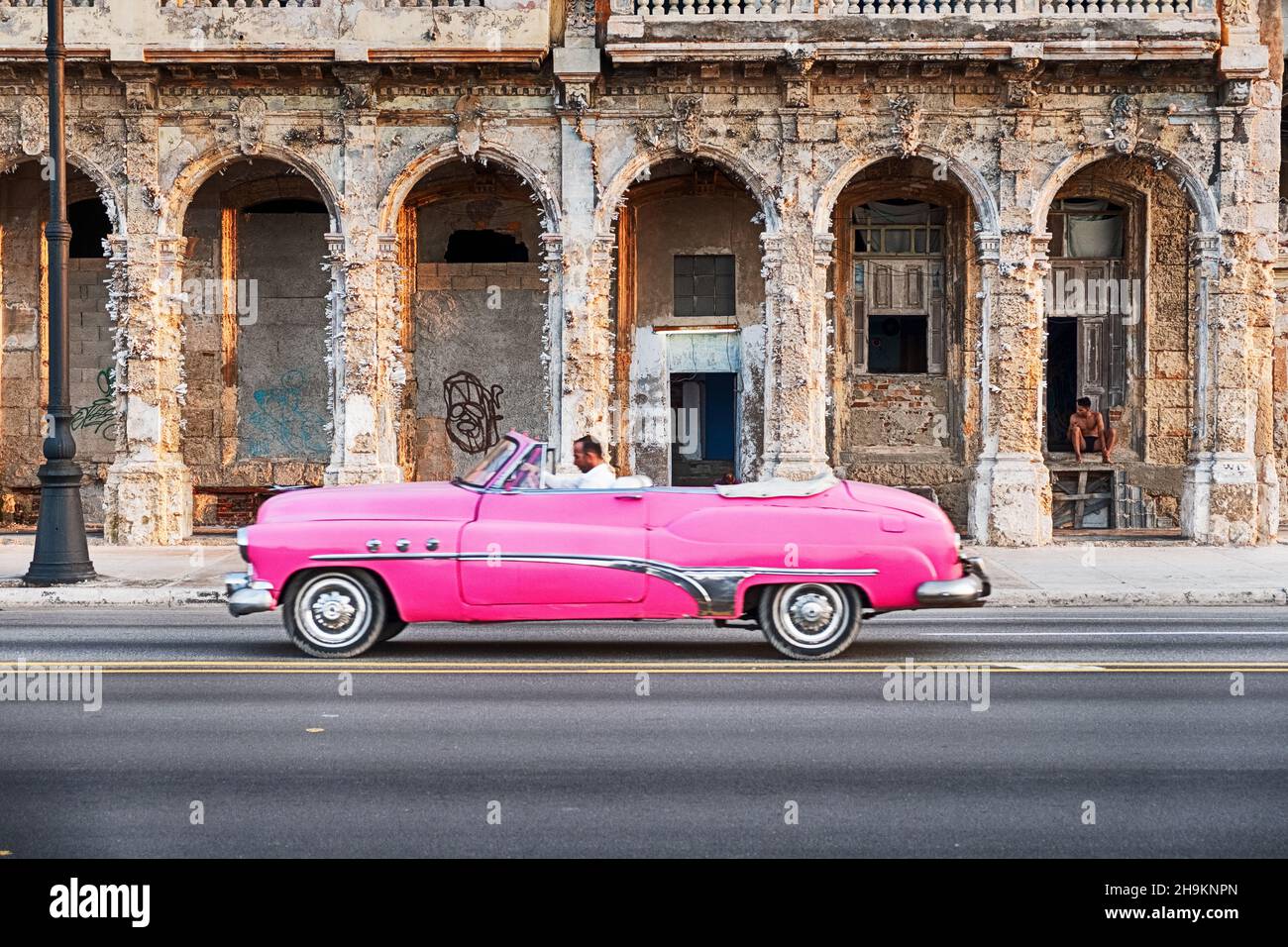 HAVANA, CUBA - DECEMBER 31, 2019: An anonymous man drives a vintage pink American convertible as a taxi on the Malecon waterfront road in front of an Stock Photo