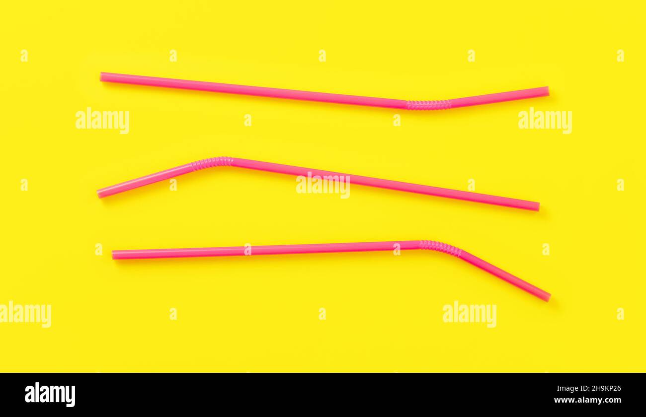 Three pink plastic drinking straws on yellow board, view from above Stock Photo