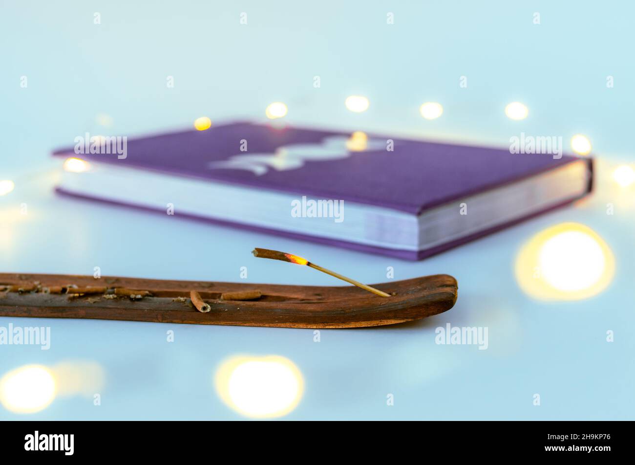 Close up incense stick burning with a moon journal with Christmas lights background. Concept: spiritual self care practices Stock Photo