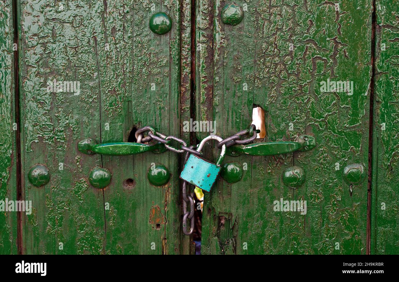 A small blue padlock locks an old green wooden door. Stock Photo