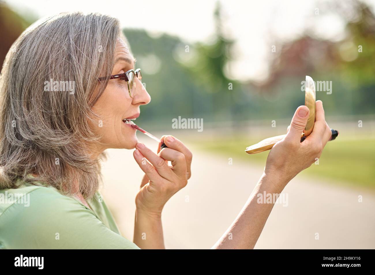 Profile of woman wearing glasses apply lipstick outdoors Stock Photo