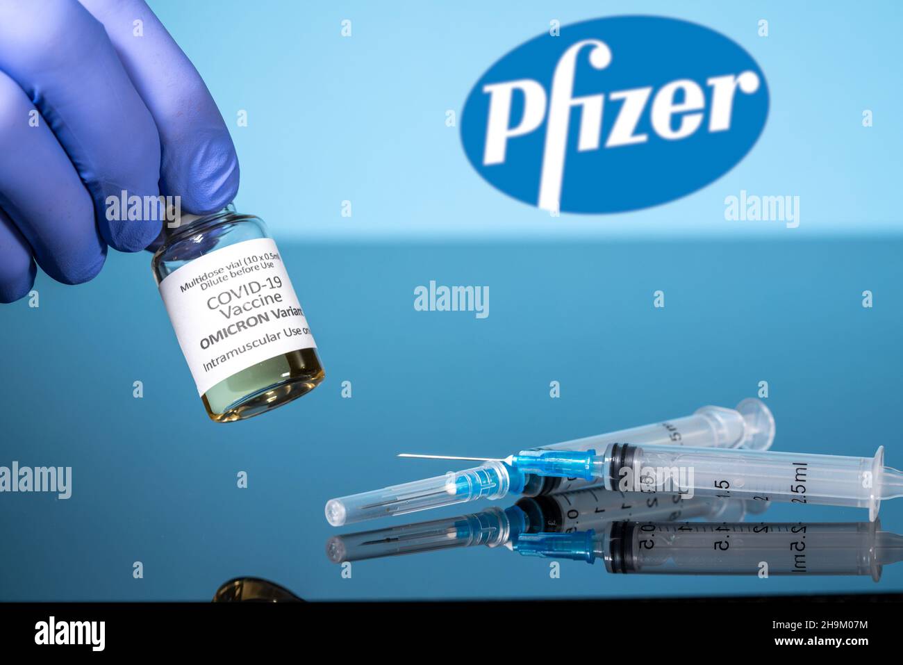 Morgantown, WV - 7 December 2021: Small bottle of coronavirus vaccine for Omicron variant with syringe with background of Pfizer logo Stock Photo