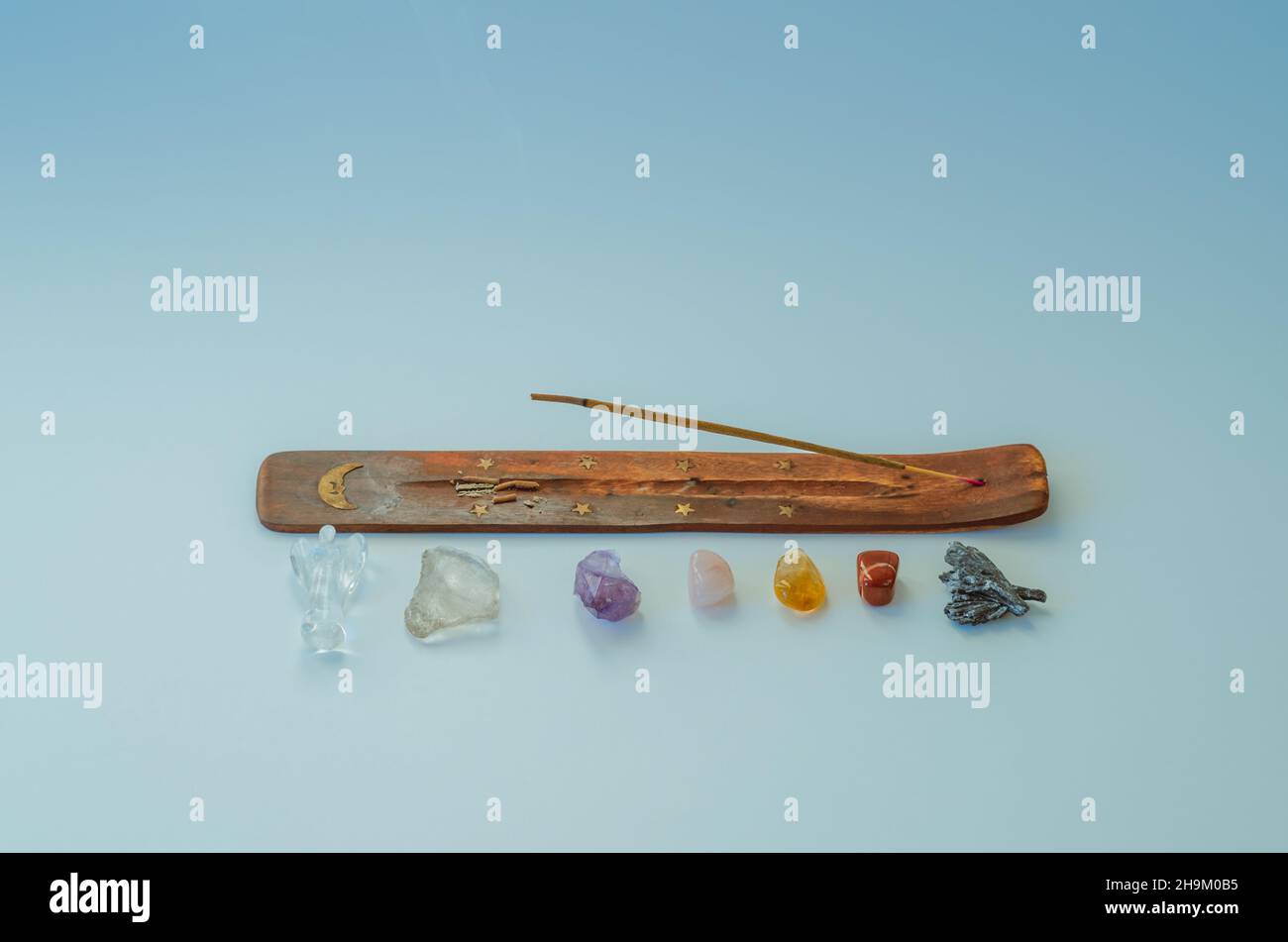 Flat lay of incense stick burning and 7 healing crystals aligned by chakra on blue background Stock Photo