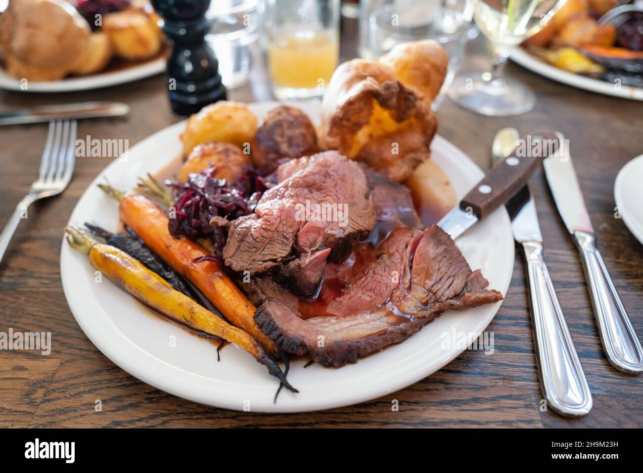 Roast beef on a white plate with roast potatoes and Yorkshire pudding with vegetables in a restaurant. Stock Photo