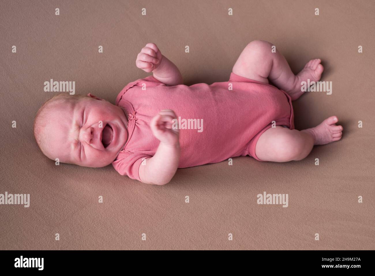 Little crying newborn baby on a brown blanket Stock Photo