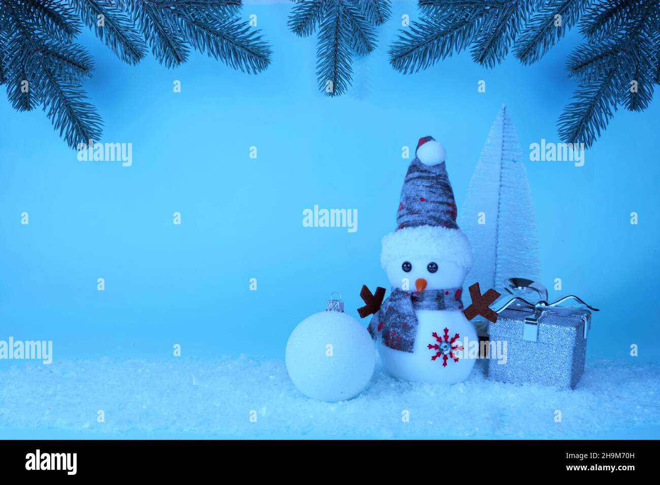 Snowman, gift, Christmas tree, Christmas ball on white snow on a blue background with Christmas tree branches and garlands. Christmas New Year card Stock Photo