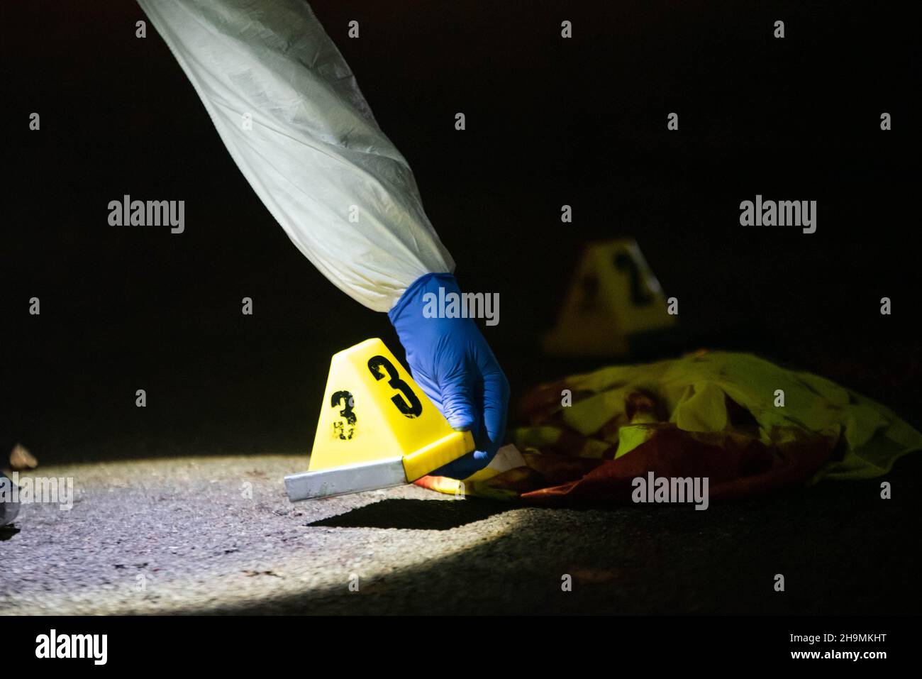 Forensics placing evidence marker number three by bloodied reflective vest, Birmingham, UK. Stock Photo