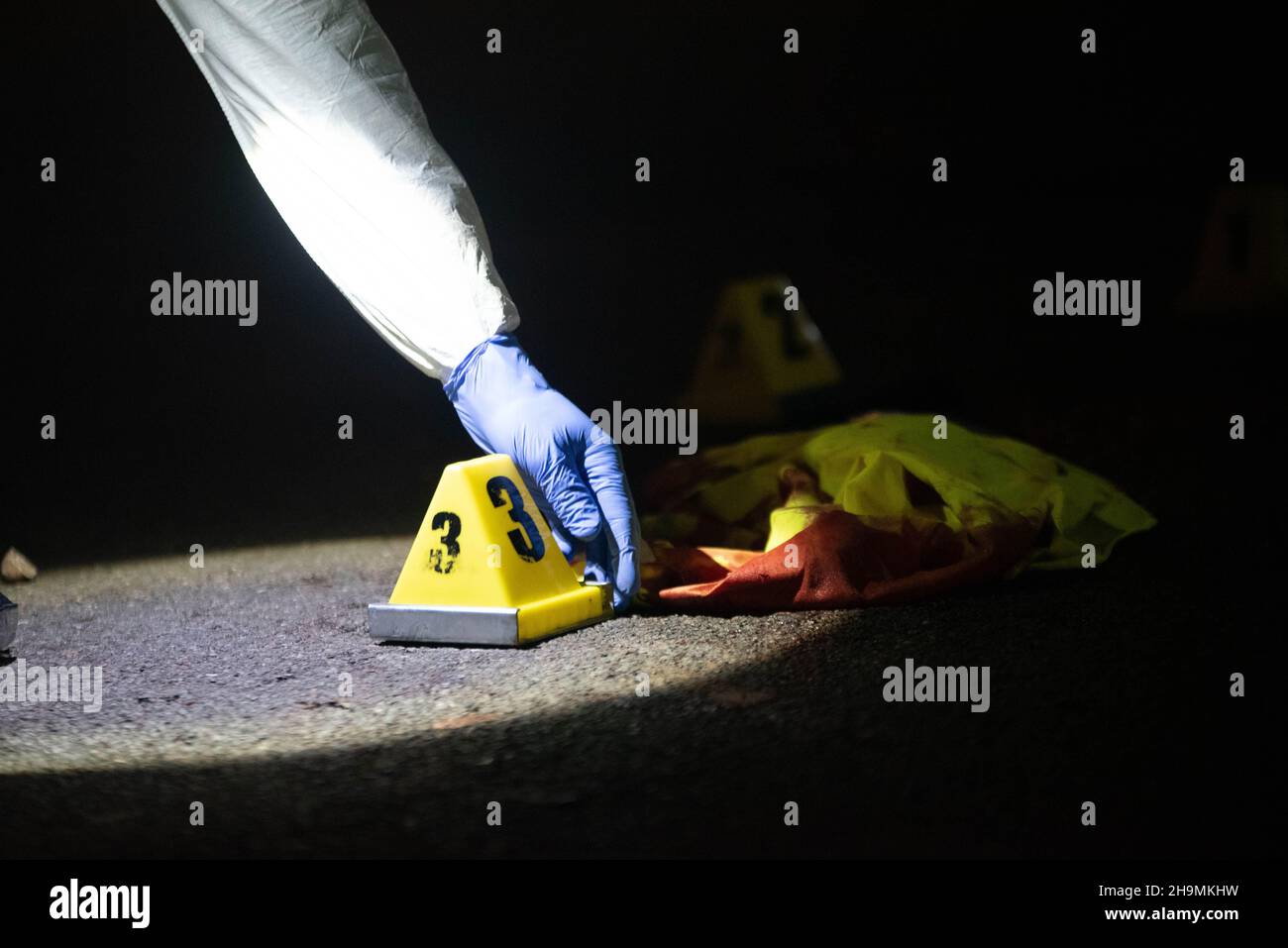 Forensics placing evidence marker number three by bloodied reflective vest, Birmingham, UK. Stock Photo