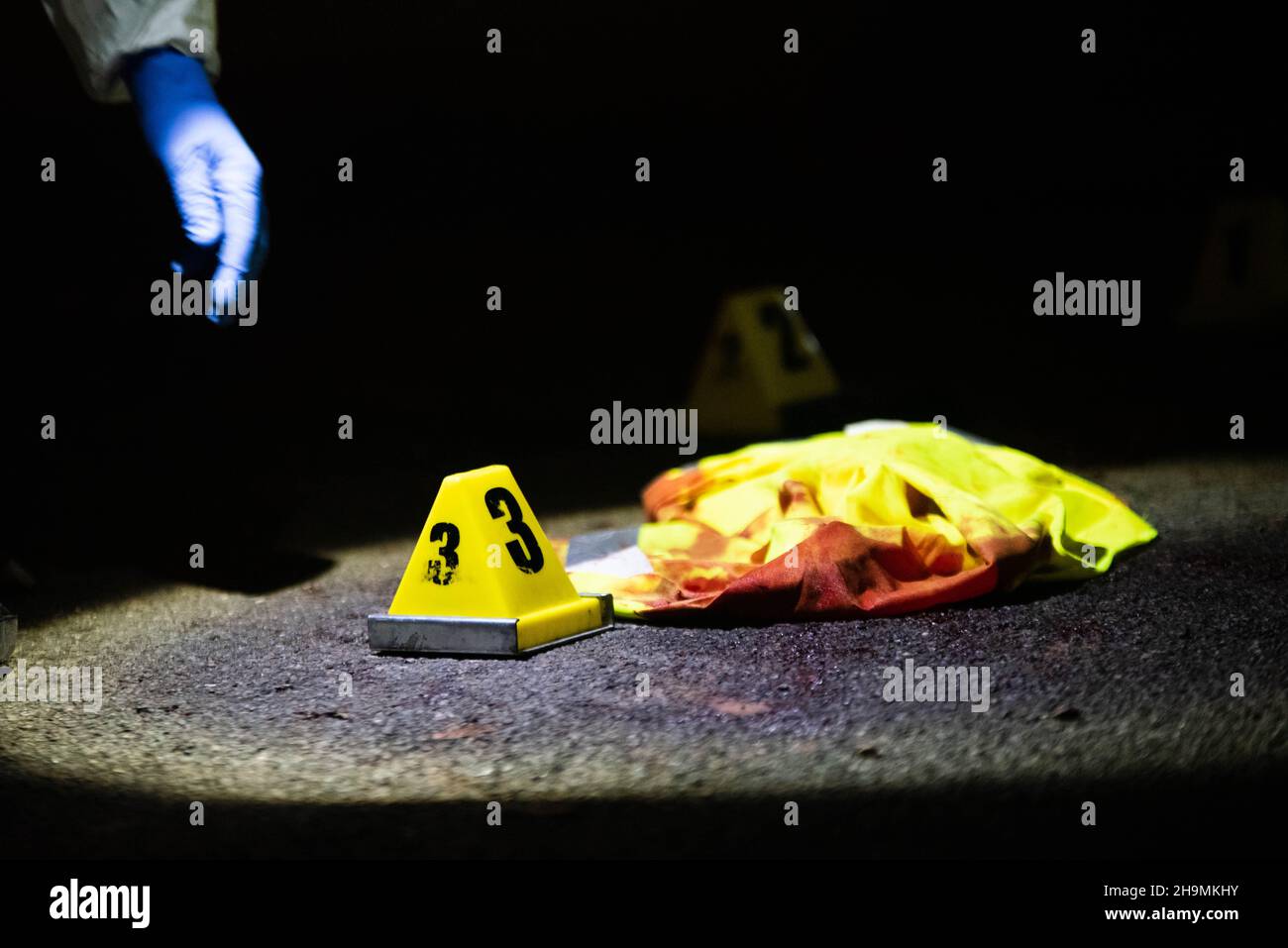 Forensics placing evidence marker number three by bloodied reflective vest, Birmingham, UK. Stock Photo