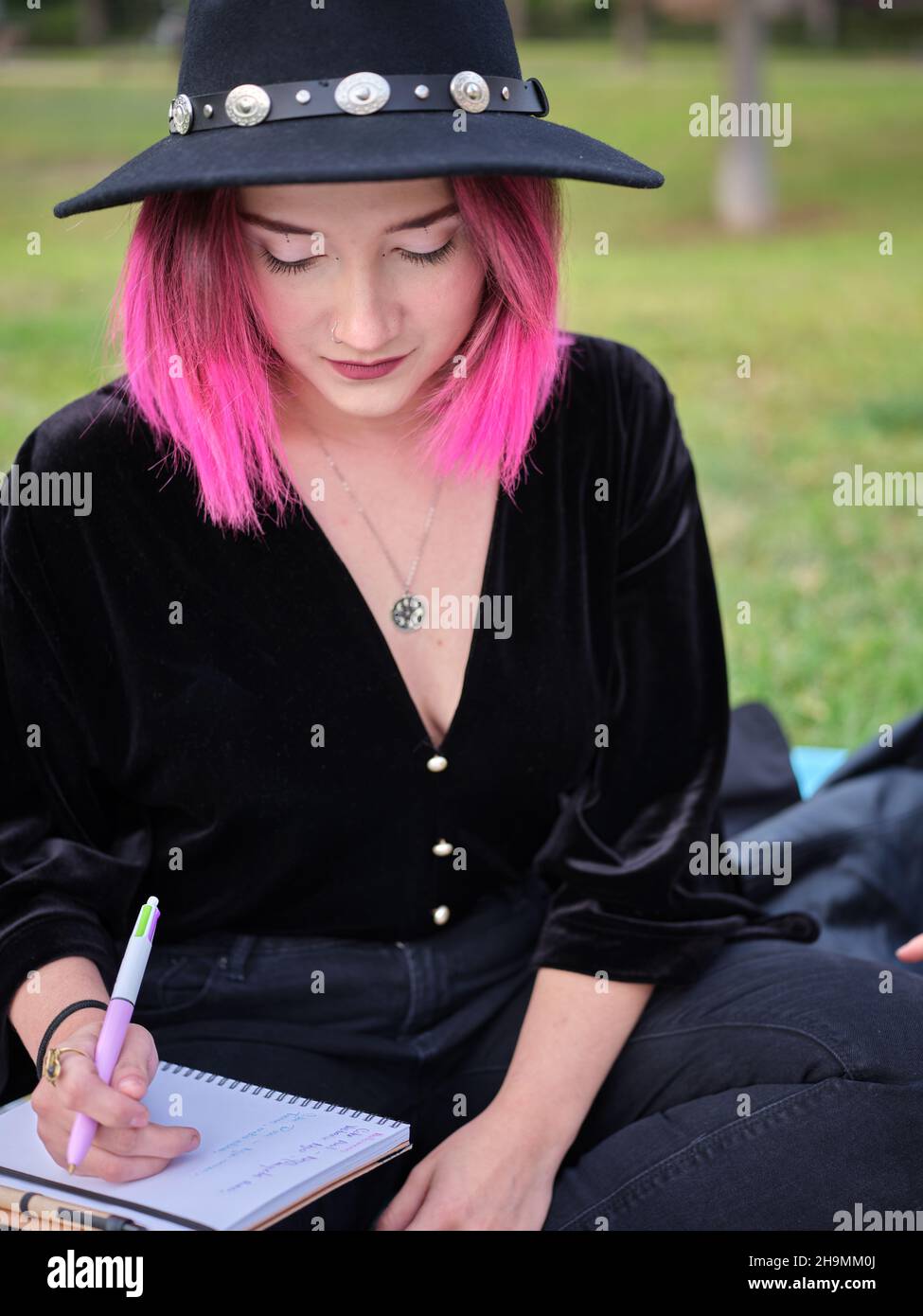 portrait of a young girl with pink hair and a black hat sitting with a notebook Stock Photo