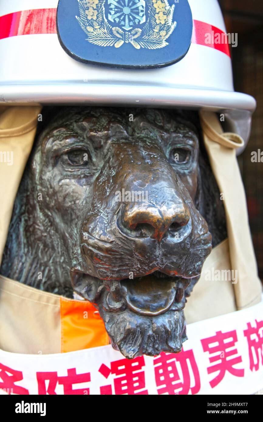 One of the bronze lion statues location at the main entrance to Mitsukoshi Department Store in Ginza, Tokyo, dressed in a fireman's uniform and helmet. Stock Photo