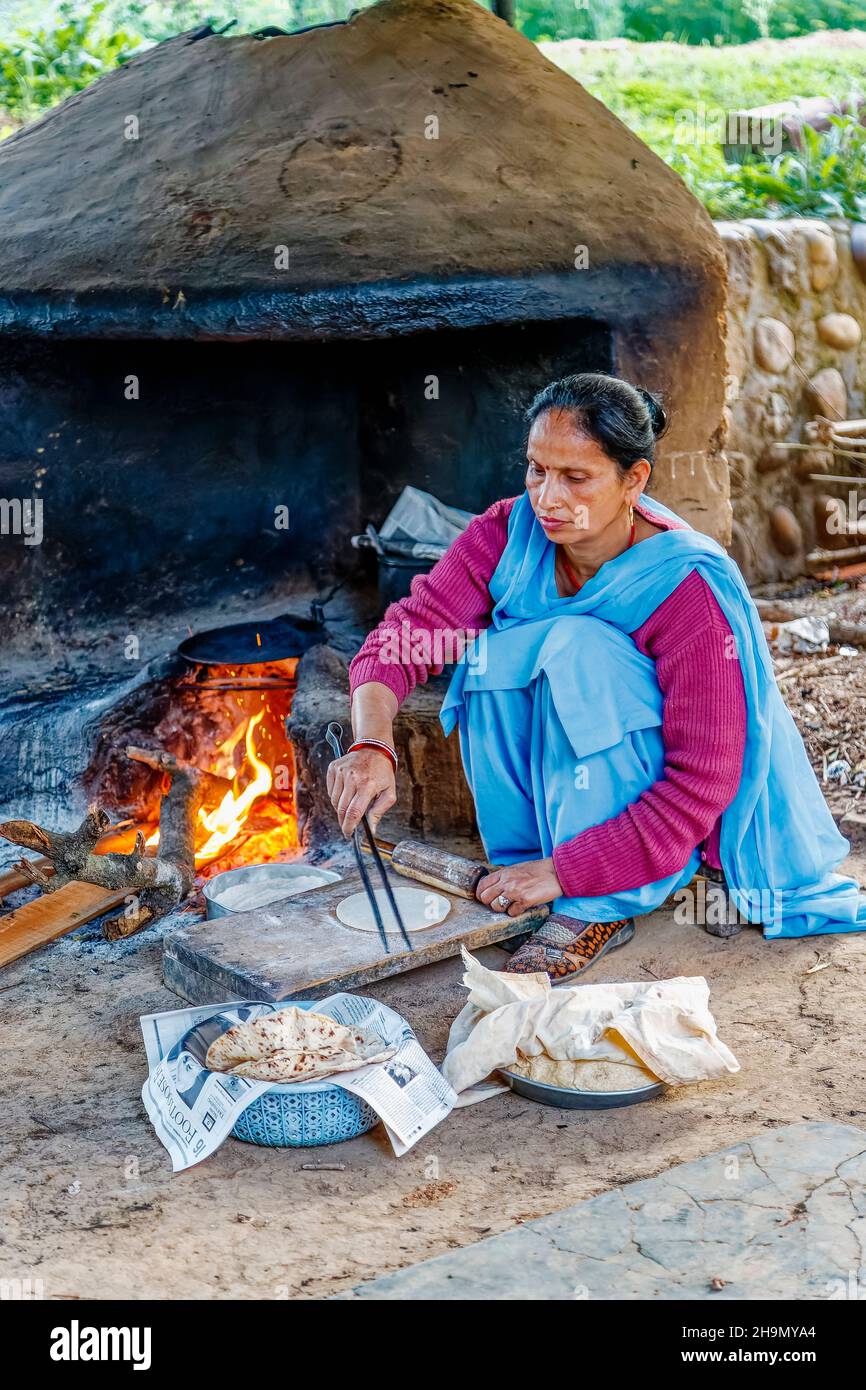 Local Indian woman wearing blue sari cooking chapatis in an oven with open fire, Judge's Court Hotel, Pragpur, Kagra district, Himachal Pradesh, India Stock Photo