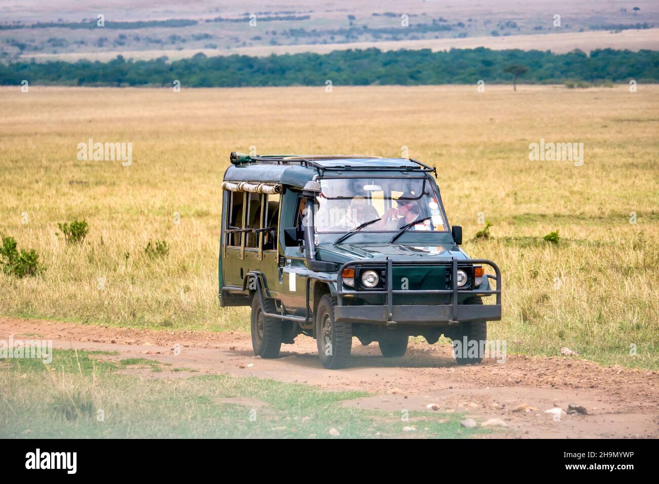 A safari vehicle on a dusty dirt track on a game drive in the Maasai Mara National Reserve in Kenya. Stock Photo