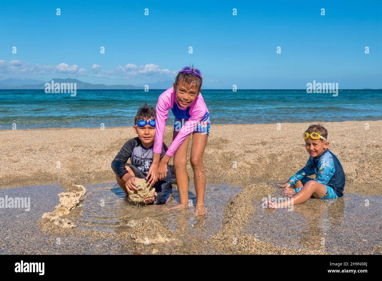 Three cute kids playing on a sandy beach on an island in the Philippines during a family summer vacation. The girl is Asian, the two boys are Eurasian Stock Photo