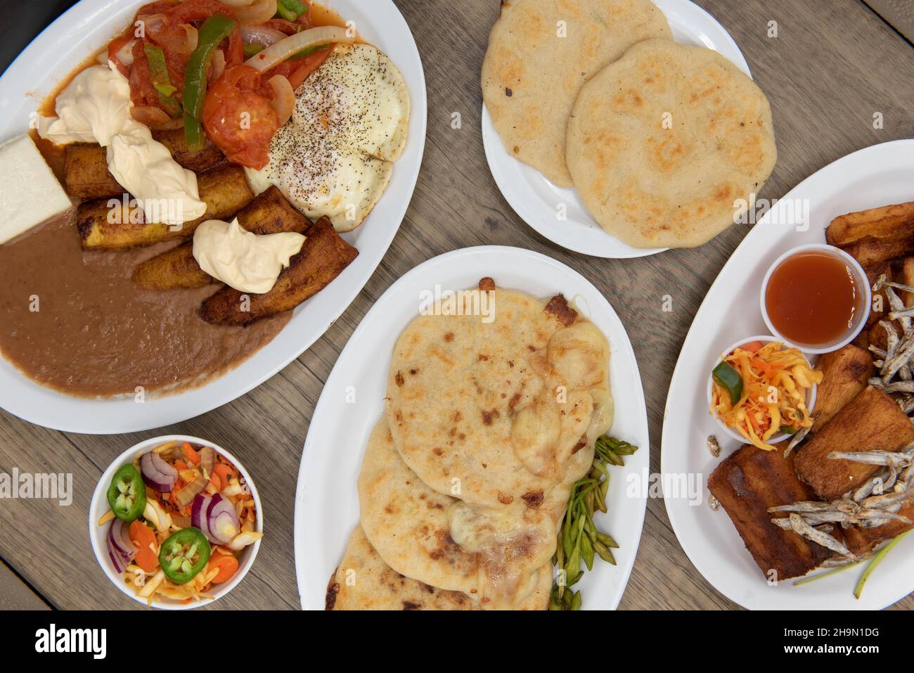 Overhead view of Latino flavored table of prepared El Salvadoran food with meat, fried plantains, pupusa, yucca, and refried beans. Stock Photo