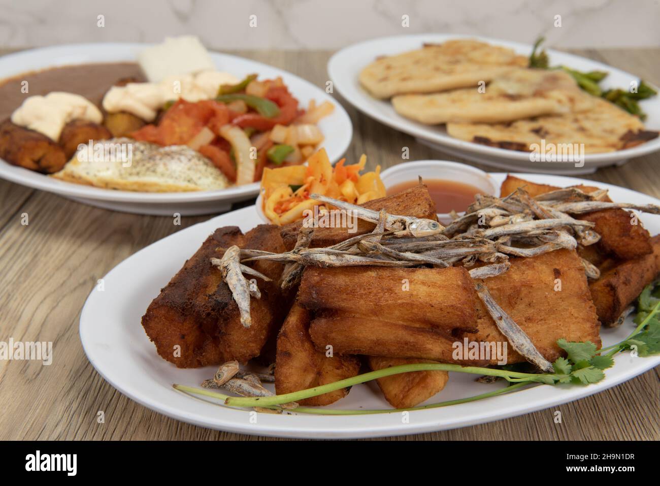 Latino flavored table of prepared El Salvadoran food with meat, fried plantains, pupusa, yucca, and refried beans. Stock Photo