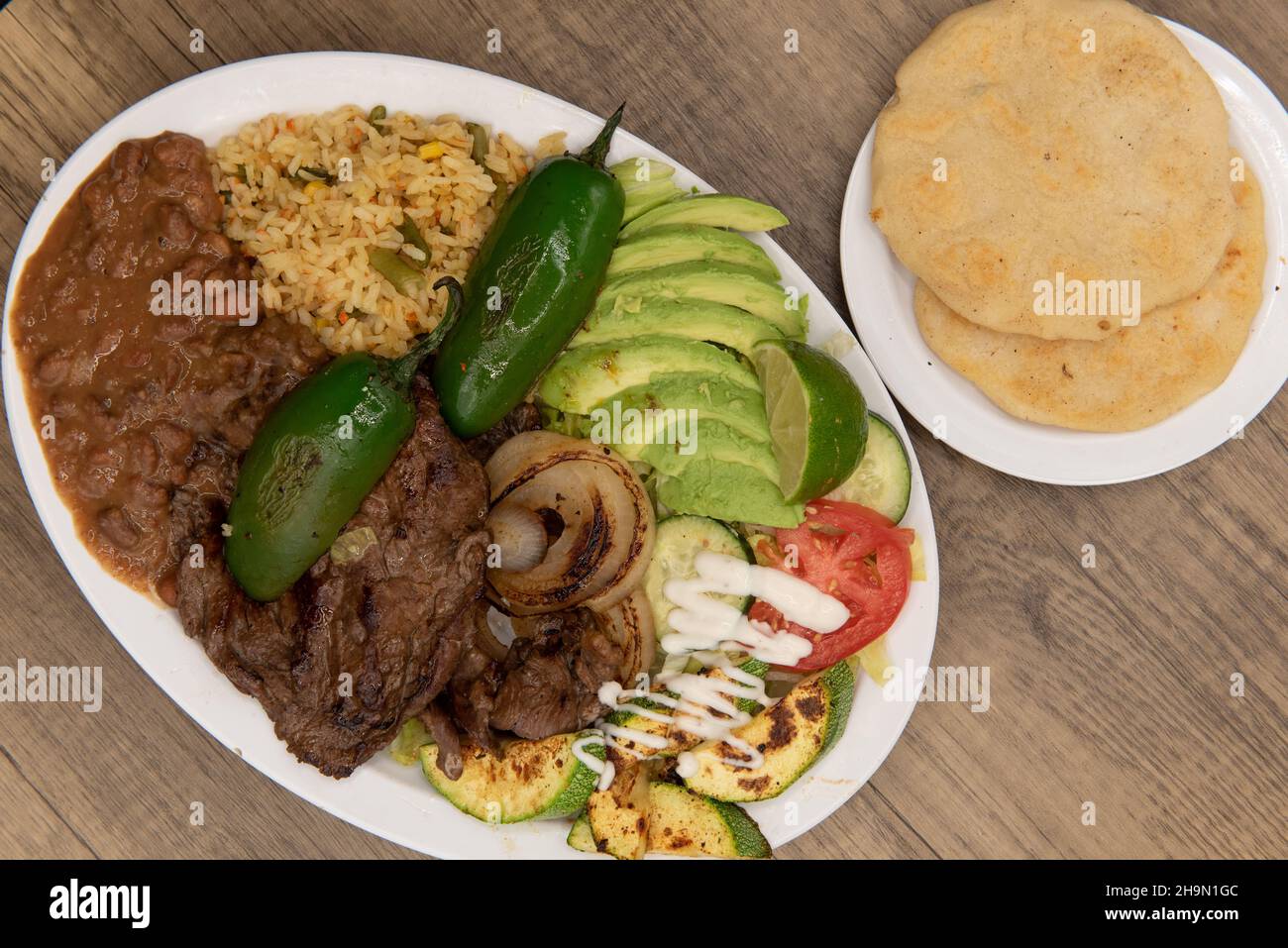 Overhead view of perfectly grilled steak on a plate with Latino rice and sliced avocados and pupusa on the side. Stock Photo