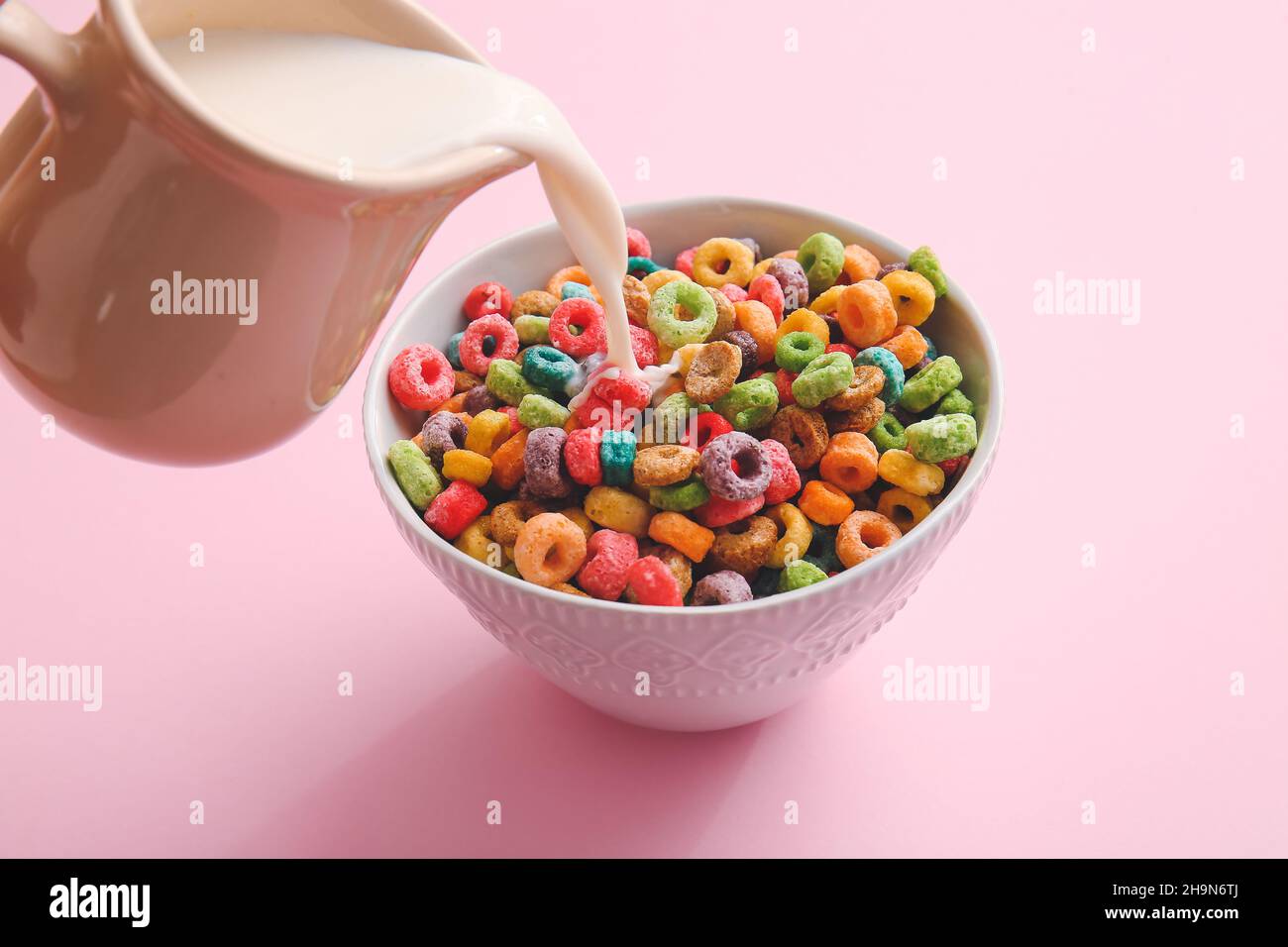 Pouring milk in bowl of colorful cereal rings on pink background Stock