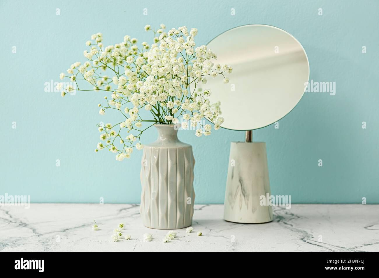 Vase with beautiful gypsophila flowers and mirror on table near color ...