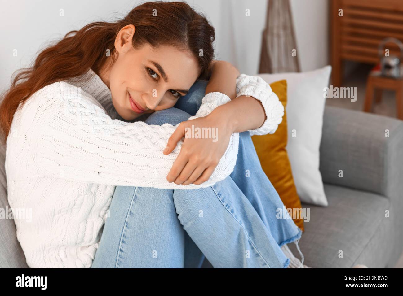 Beautiful young woman sitting on sofa at home Stock Photo - Alamy