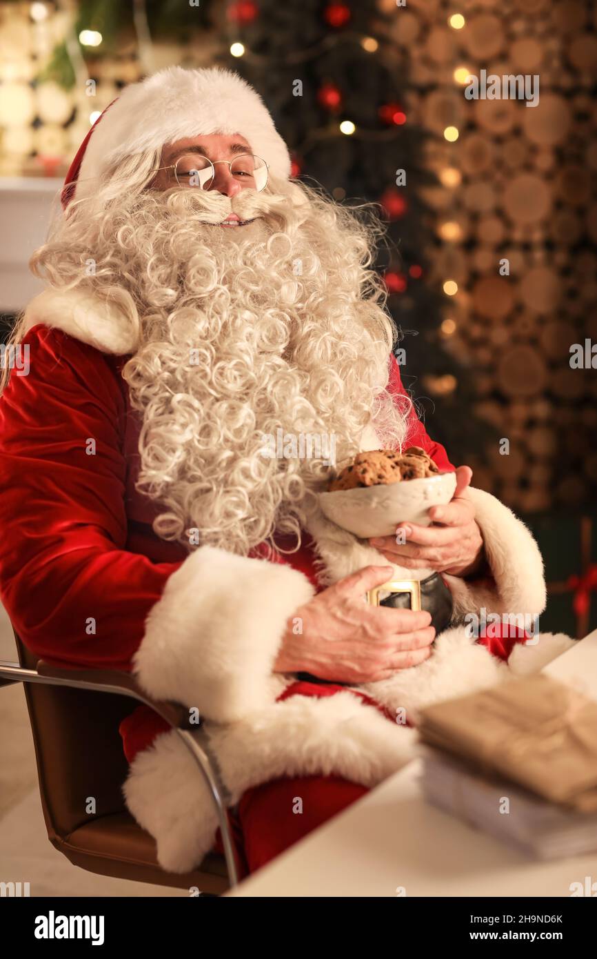 Happy Santa Claus with tasty cookies at home in evening Stock Photo