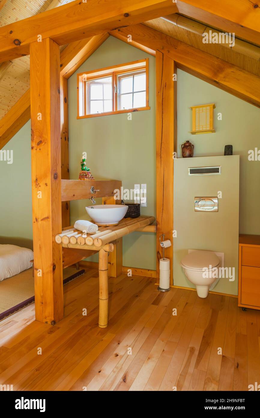 Ensuite with bamboo wood vanity and wall-mounted toilet in open concept design principal bedroom on upstairs floor inside timber frame home. Stock Photo