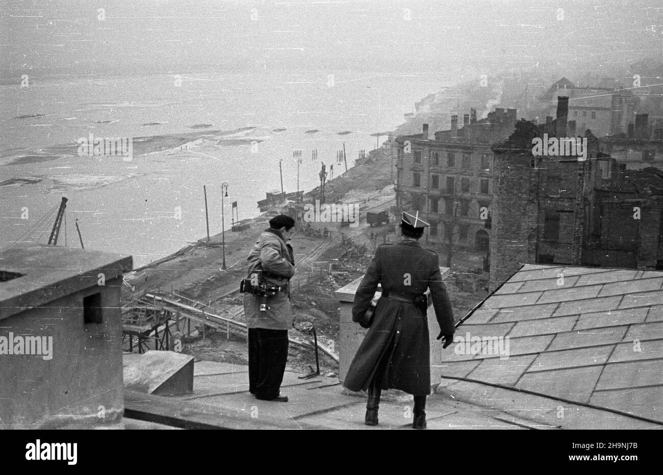 Warszawa, 1948-12. Odbudowa Mariensztatu i Wybrze¿a Koœciuszkowskiego. Nz. fotoreporter Polskiej Kroniki Filmowej W³adys³aw Forbert w asyœcie oficera Wojska Polskiego podczas zdjêæ na dachu gmachu przy ulicy Nowy Zjazd 1; widok w górê Wis³y.  mta  PAP    Dok³adny dzieñ wydarzenia nieustalony.      Warsaw, Dec. 1948. The rebuilding of Mariensztat and Wybrzeze Kosciuszkowskie. Pictured: Polish Newsreel cameraman Wladyslaw Forbert, accompanied by a Polish Army offcier filming on a roof of a building at 1 Nowy Zjazd Street; a view of the Vistula River.   mta  PAP Stock Photo